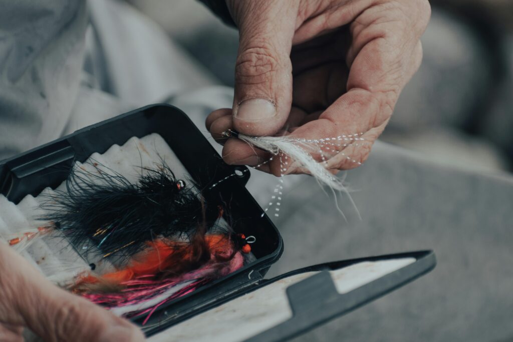 Detailed view of a hand holding a fly fishing lure from a box, depicting preparation for fishing.